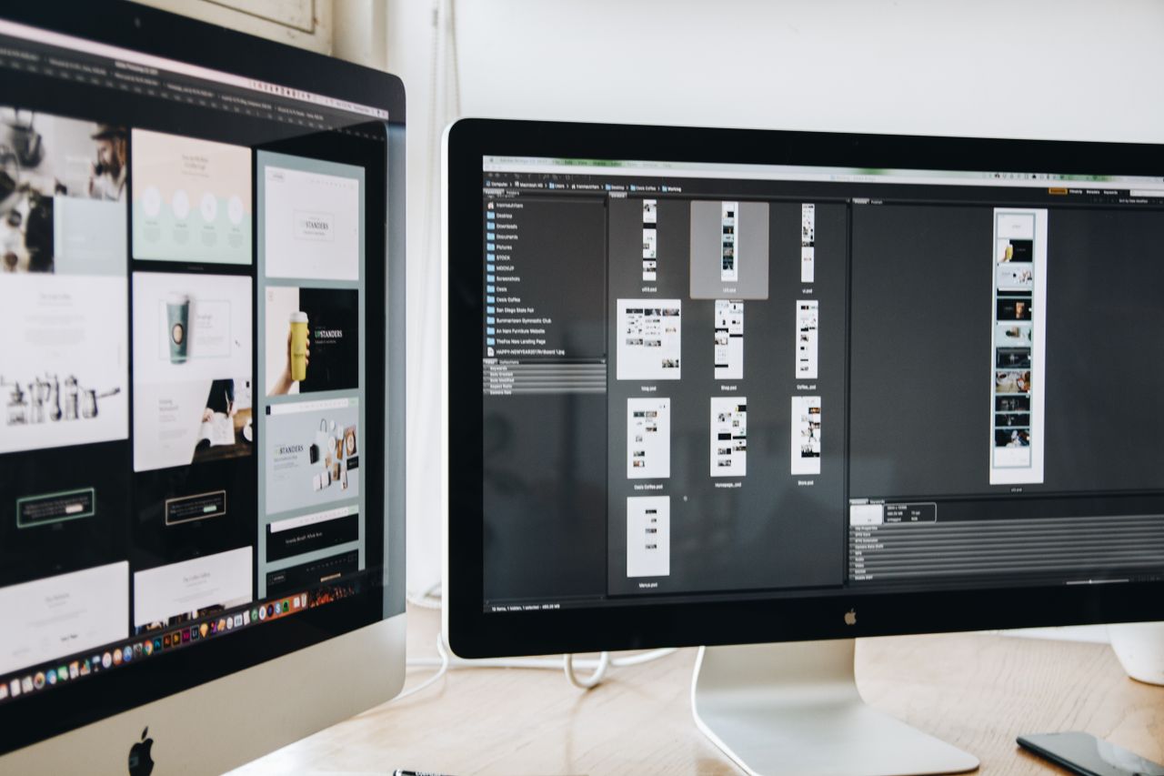 Moderní pracovní prostor s dvěma počítačovými monitory zobrazujícími webdesignové projekty, který zdůrazňuje technologie a produktivitu.